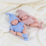 Two baby dolls in blue and pink outfits lying on a soft surface.