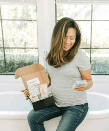 Pregnant woman relaxing on a couch with her morning sickness survival box of pregnancy relief products.
