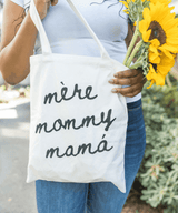 Person holding a tote bag with 'mère mommy mamá' text.