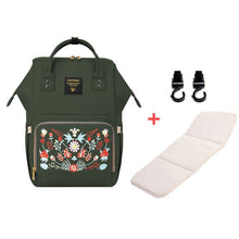 Green backpack with floral embroidery, white mat, and black hooks