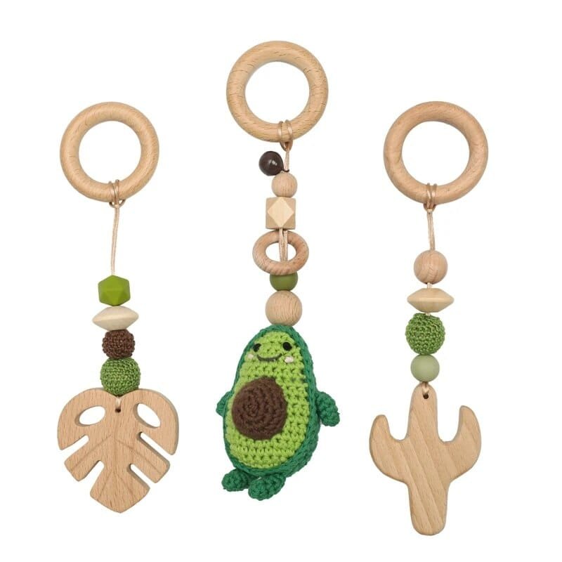 Three wooden baby teething toys with avocado, leaf, and cactus designs on a white background.
