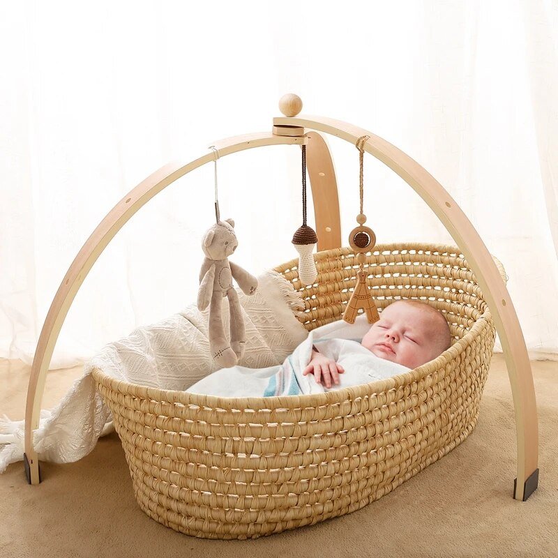 Natural wood baby play gym set over a bassinet with sensory hanging toys for calm newborn rest and play.