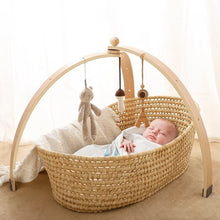 Natural wood baby play gym set over a bassinet with sensory hanging toys for calm newborn rest and play.