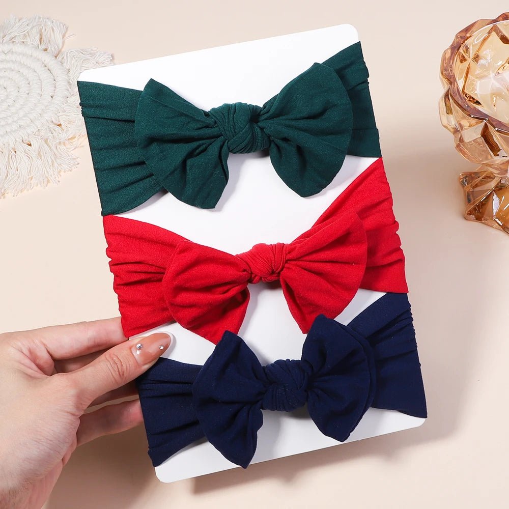 Three fabric bows in green, red, and blue on a white tray with a hand holding the tray.