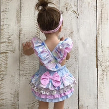 Child wearing a colorful dress with ruffles and bows.