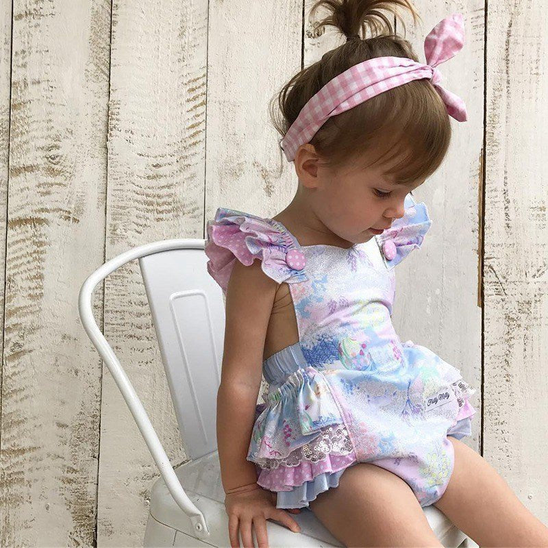 Child wearing a colorful, floral romper with ruffles.