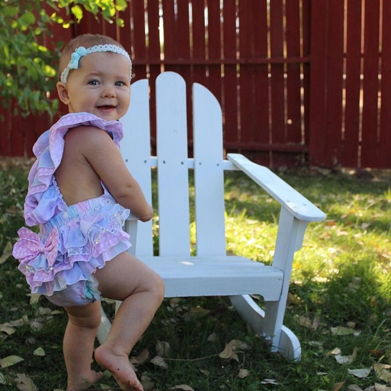 Baby in a colorful outfit sitting on a white chair outdoors.