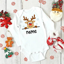 White baby onesie with reindeer design and 'name' text, surrounded by Christmas decorations on a wooden surface. (option 28)