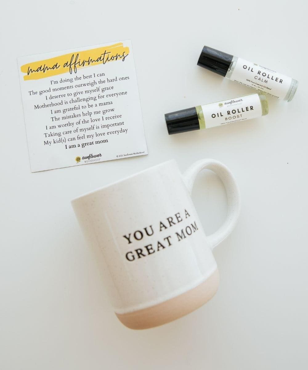 Mug with 'You are a great mom' text, oil roller bottles, and an affirmation card.