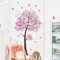 Pink butterfly and flower tree wall decal applied to a white wall for nursery decorating and girls bedroom styling.
