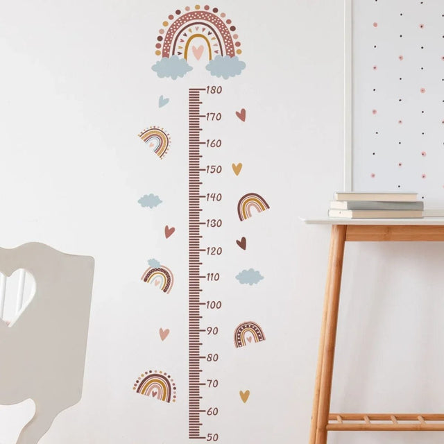 Height chart with rainbow and cloud design on a wall next to a wooden table.