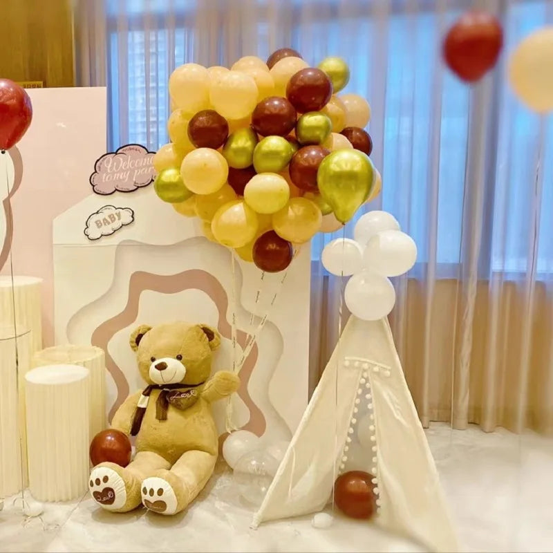 Pink teddy bear plush surrounded by balloons and a teepee for nursery party decor.