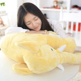 Woman lying on a large yellow shark-shaped pillow in a cozy room.
