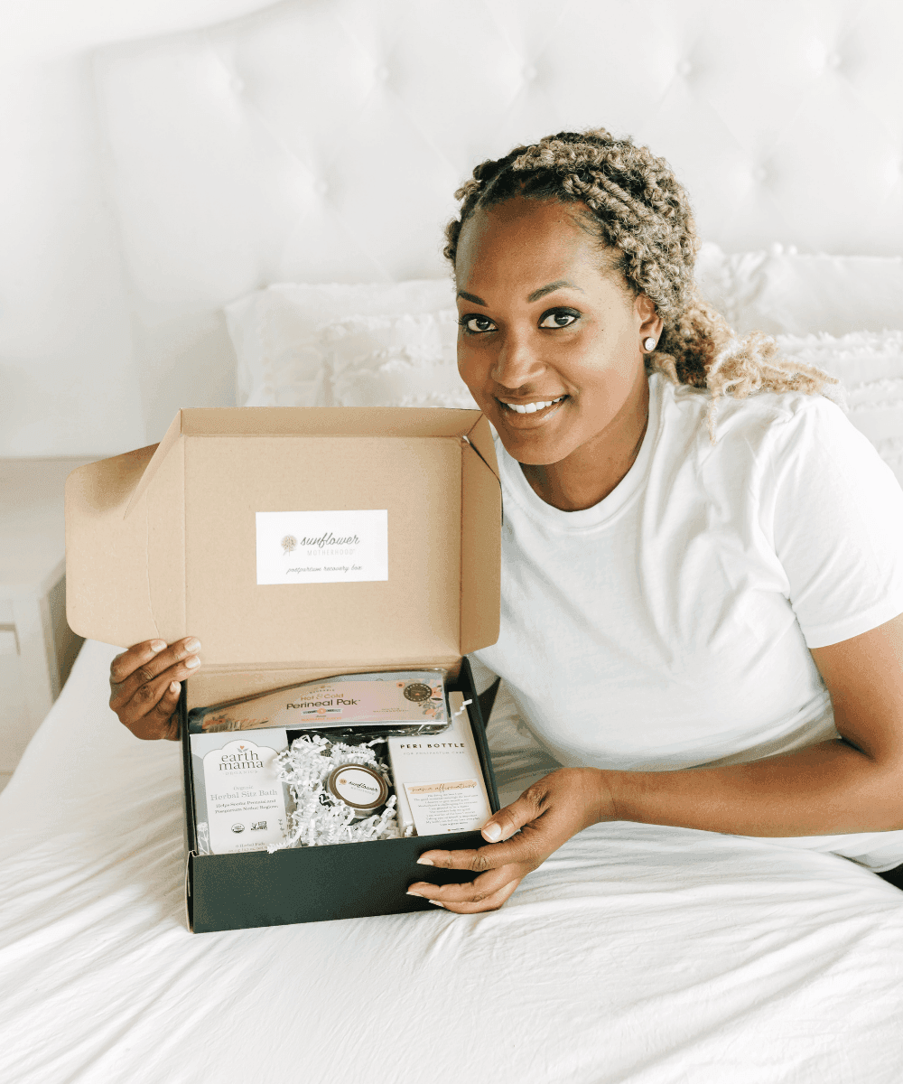 Woman holding a box with a visible brand logo, sitting on a bed.