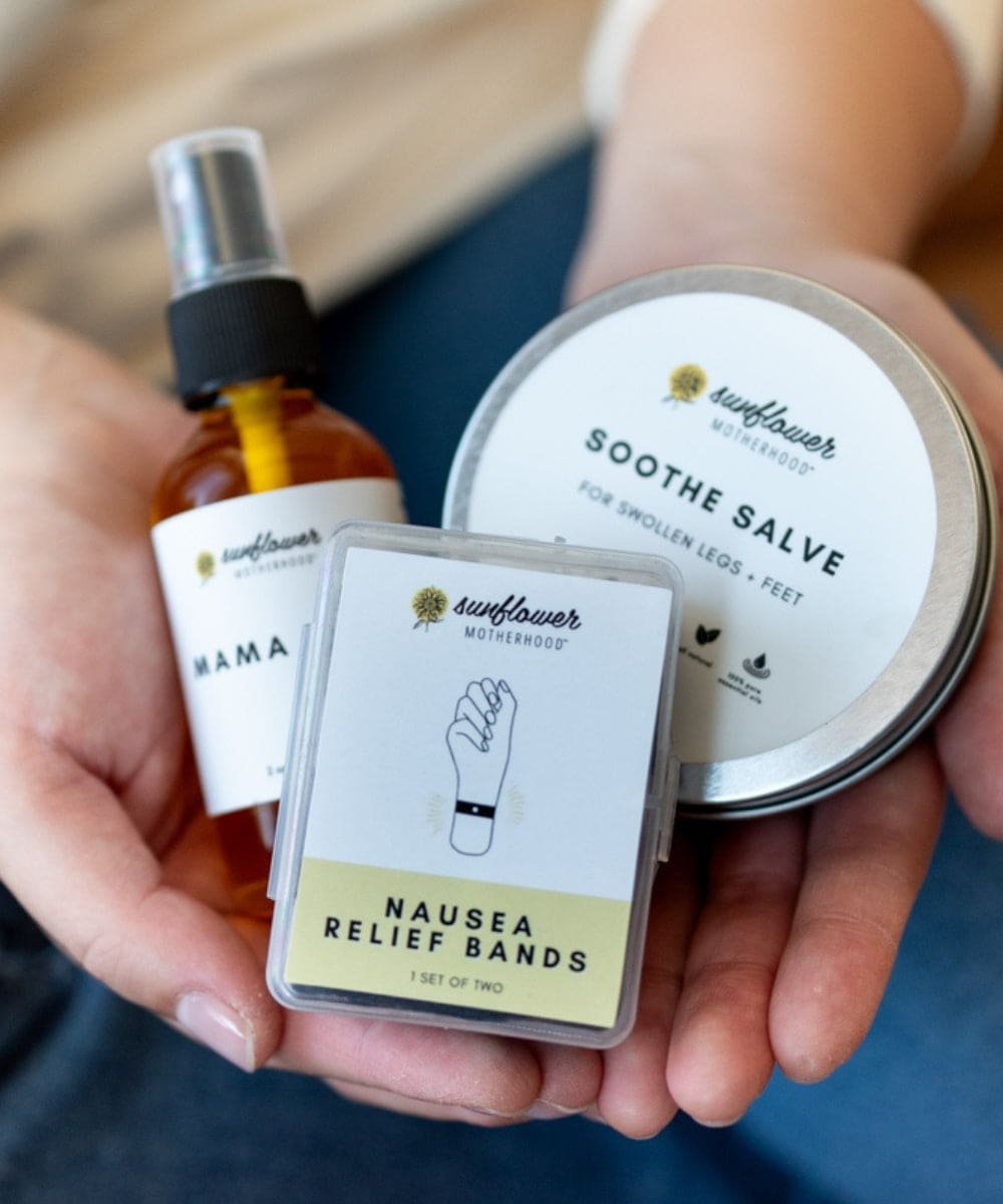 Hand holding Sunflower Naturals products including a bottle, salve jar, and nausea relief bands.