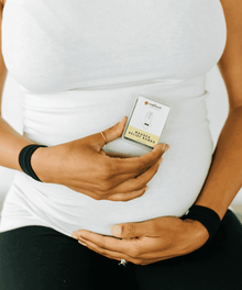 Pregnant woman holding a nausea relief bands box against her bump for pregnancy comfort and baby shower gifting.