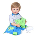 Premium Reborn Baby Boy doll with two colour hair posed with a green dinosaur toy and blanket for cosy play and photography.