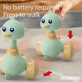 Two green press-and-swing duck toys with a hand pressing one and a no battery required note