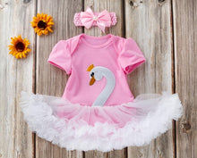 Pink baby outfit with swan design, tutu, and headband on a wooden background