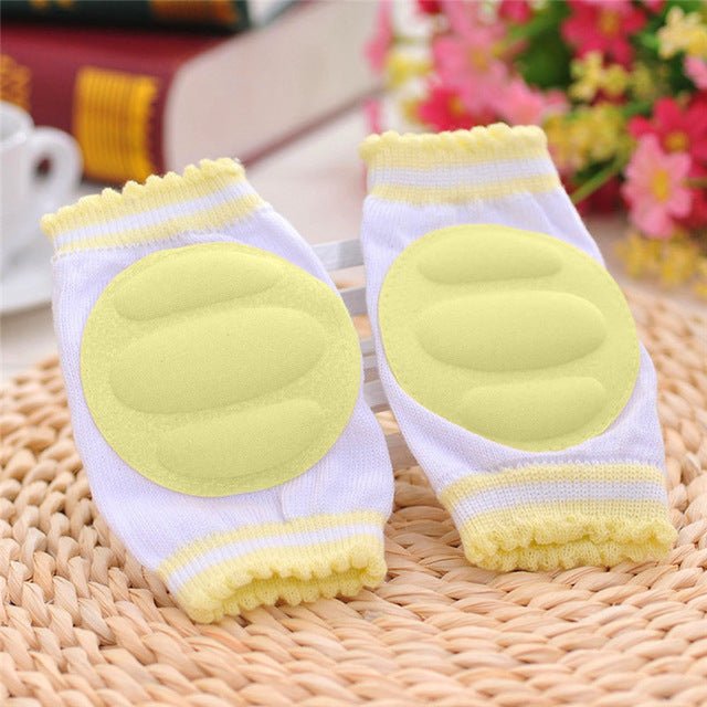 Pair of white knee pads with yellow padding on a woven surface.