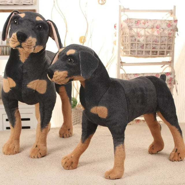 Two Doberman pinscher plush toys standing on a carpeted floor.