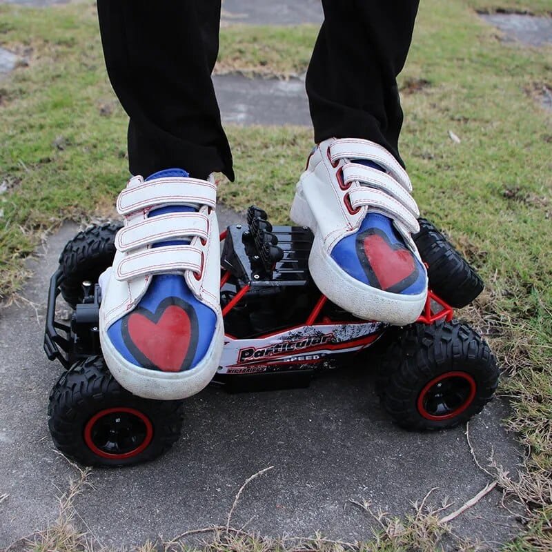 Person wearing white sneakers with blue and red hearts on a small remote-controlled car.