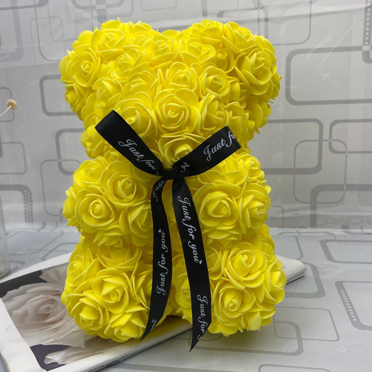Yellow rose teddy bear with a black ribbon on a gray surface