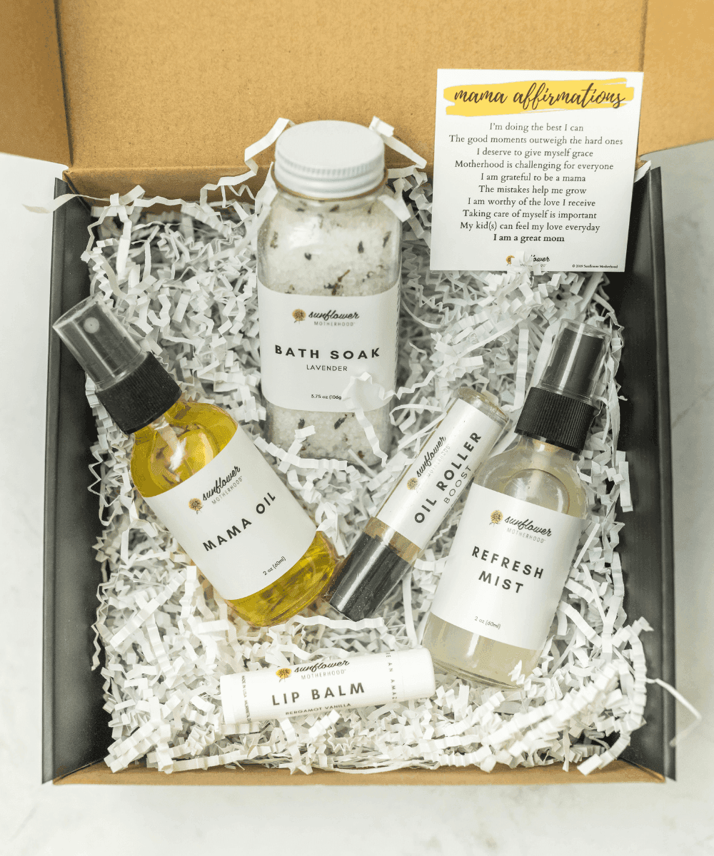 Set of self-care products including bath soak, oil roller, mist, and lip balm in a box with a card.