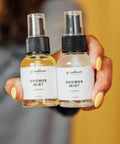 Two shower mist bottles labeled 'Morning' and 'Evening' are held by a hand with yellow nail polish.
