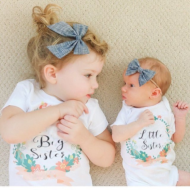 Two children wearing 'Big Sister' and 'Little Sister' shirts with floral designs.