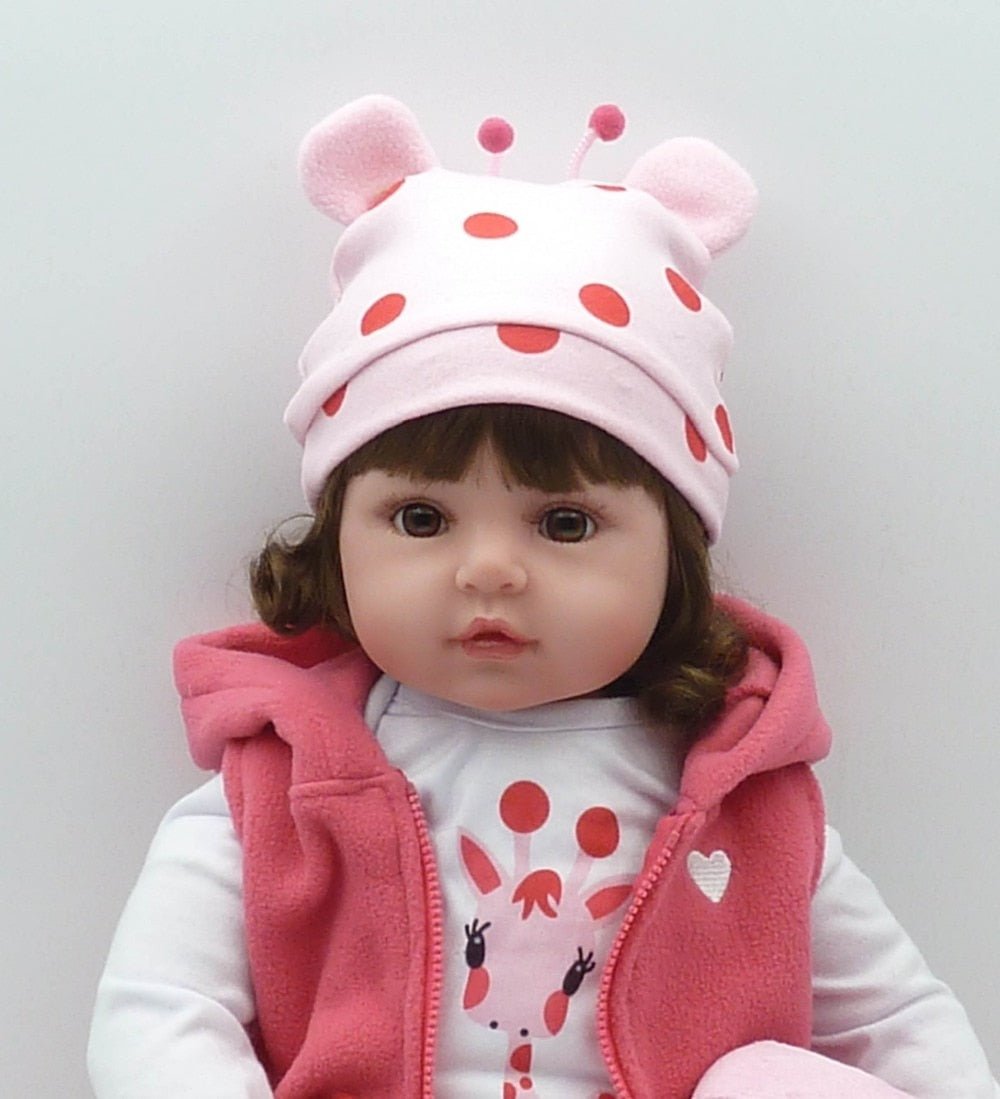 Silicone reborn toddler doll in a pink hat and outfit with realistic blushing tones for display and gentle handling.