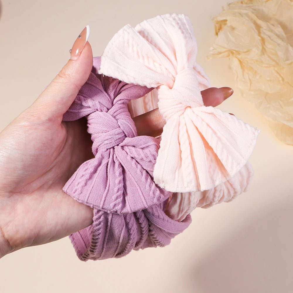 Hand holding two scrunchies, one pink and one white, against a neutral background.