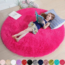 Child reading a book on a large pink round rug in a room.