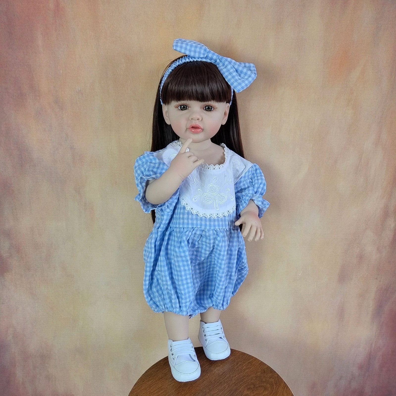 Soft silicone Reborn Baby Girl Doll with long hair in a blue checkered bow dress for dressing up and doll collecting.
