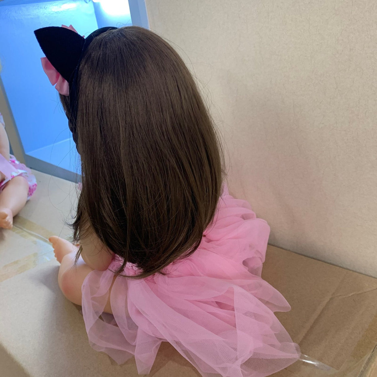 Child wearing a pink dress and black cat ears sitting on a floor.
