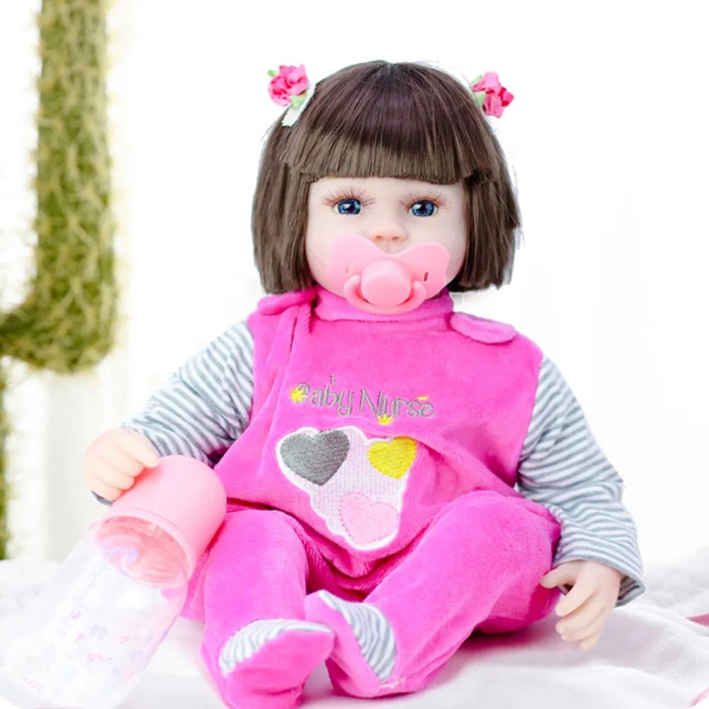 Toy doll in a pink outfit with a pacifier, sitting on a white surface.