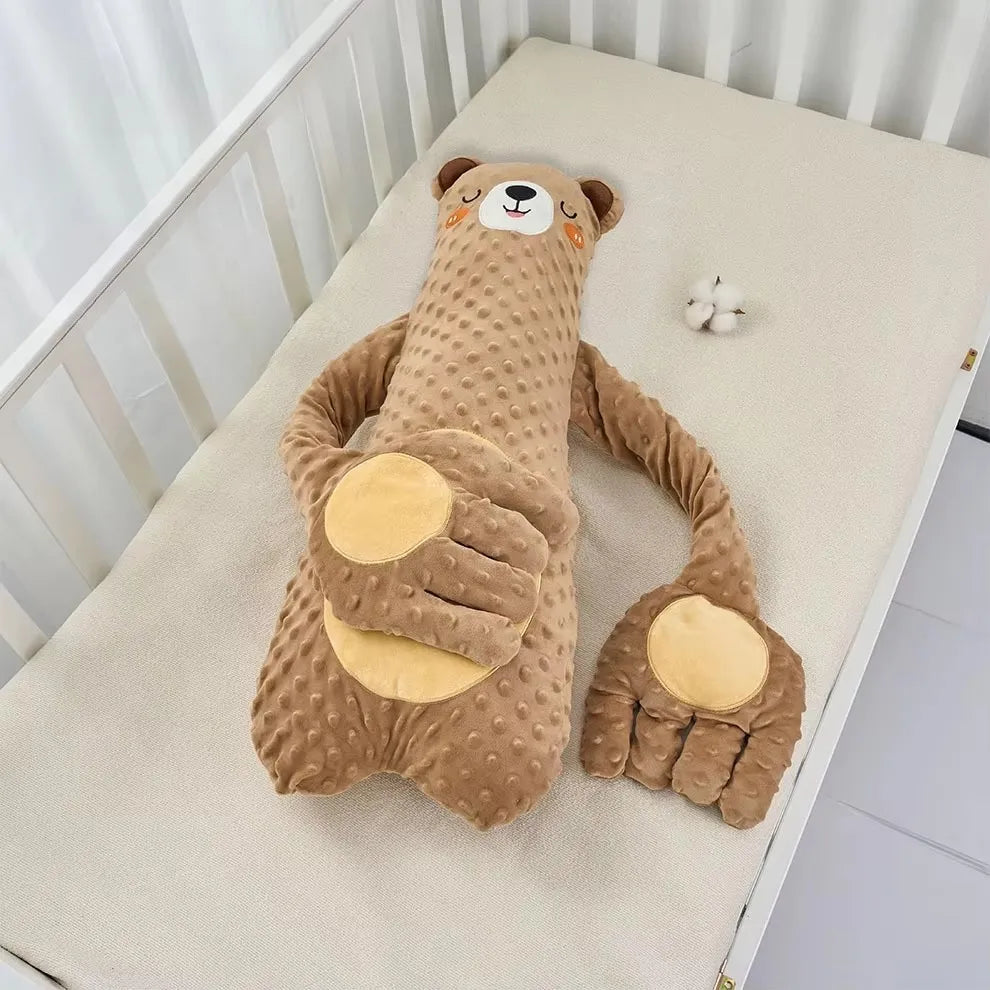 Brown bear plush pillow with long arms and tan palms laid on a crib mattress