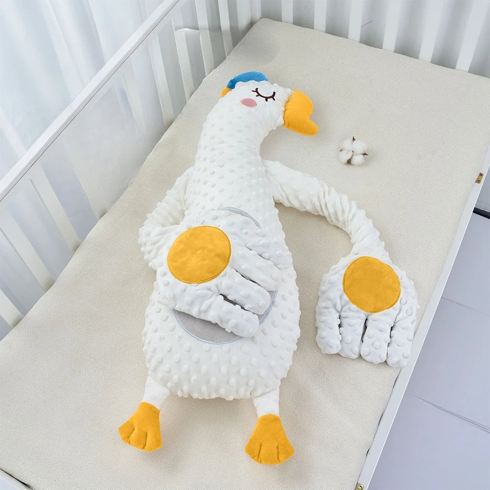 White goose plush pillow with spread orange feet on a crib mattress, second view