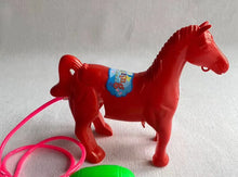 Red plastic horse toy with a pink tube and a green bulb on a grey surface
