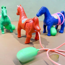 Teal, orange and blue plastic horse toys with a pink tube and a mint bulb in the foreground