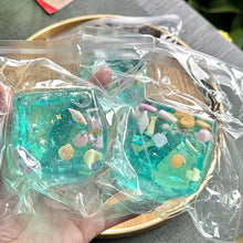 Two clear plastic packages containing blue jelly treats with sea-themed decorations on a wooden surface.