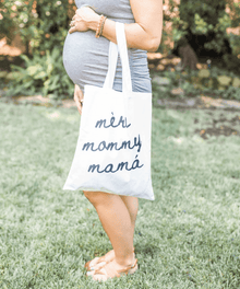 Person holding a tote bag with 'més mommy máná' text.