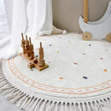 Round white rug with colorful polka dots and tassels, featuring a wooden toy on top.