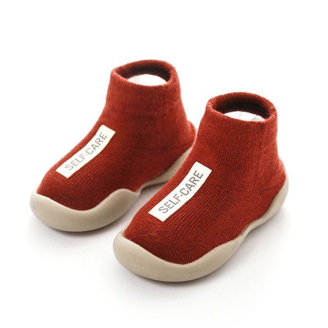 Red baby shoes with 'SELF-CARE' label on a white background