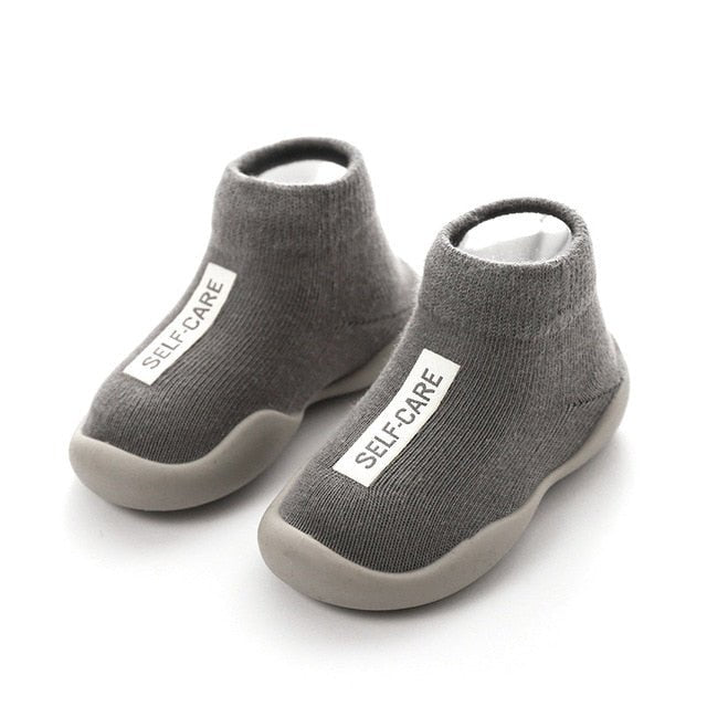 Gray children's shoes with 'SELF-CARE' label on a white background