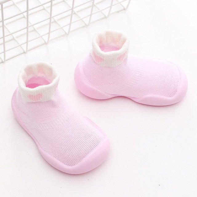 Pair of pink baby shoes with white soles on a light background