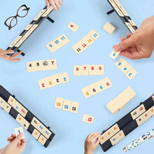 Overhead view of players with racks and tiles on a blue table, with a pair of glasses beside them