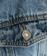 Close-up of a button on a denim jacket with a brand logo.