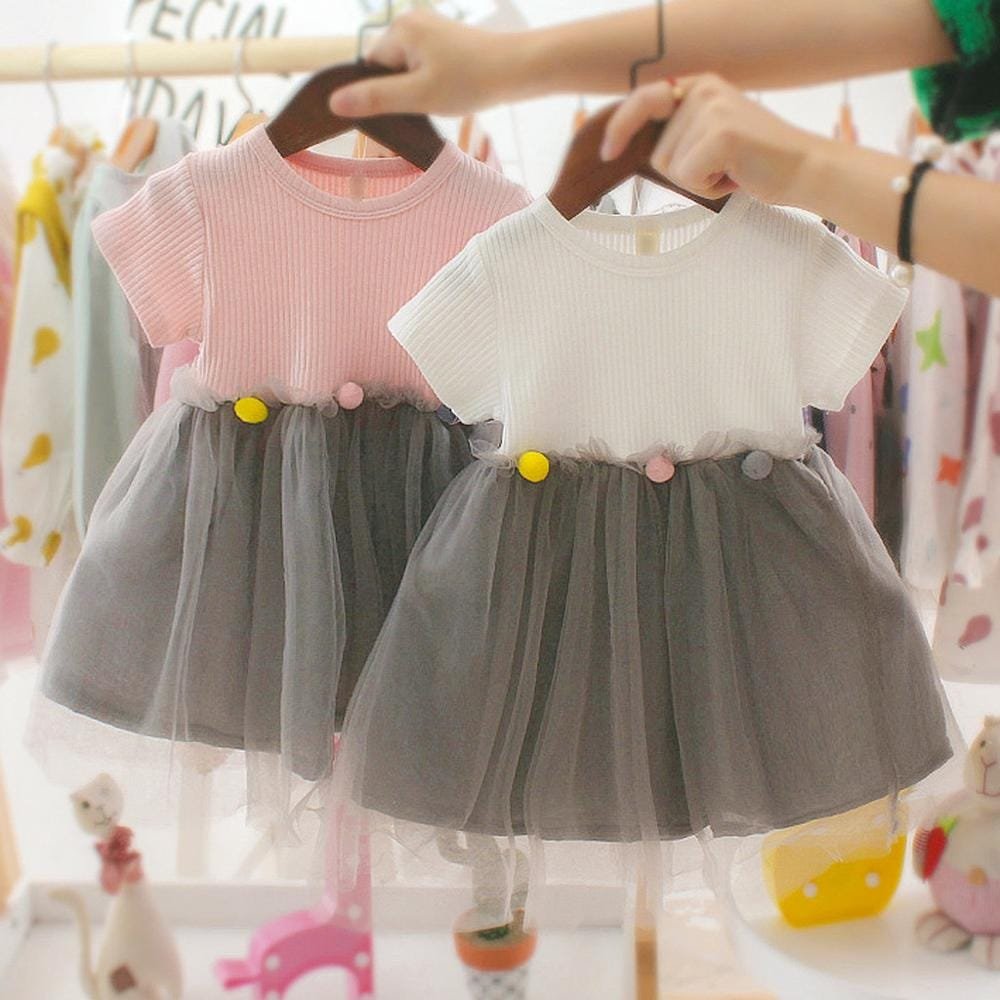 Two toddler girls tulle pom pom dresses side by side for comparing colours before choosing a party outfit.