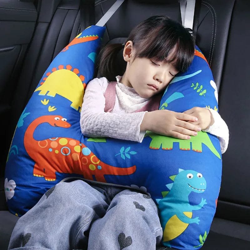 Child sleeping on a dinosaur-patterned car seat pillow in a vehicle.